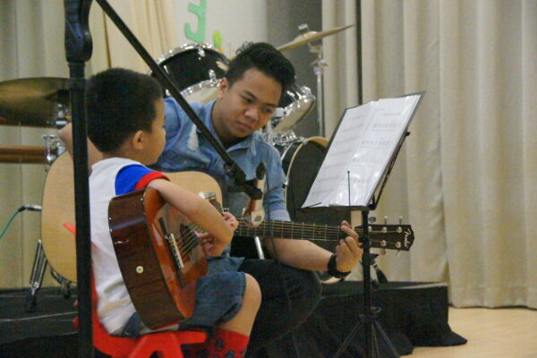 Fine momentum instructor teaching music class student how to play the guitar